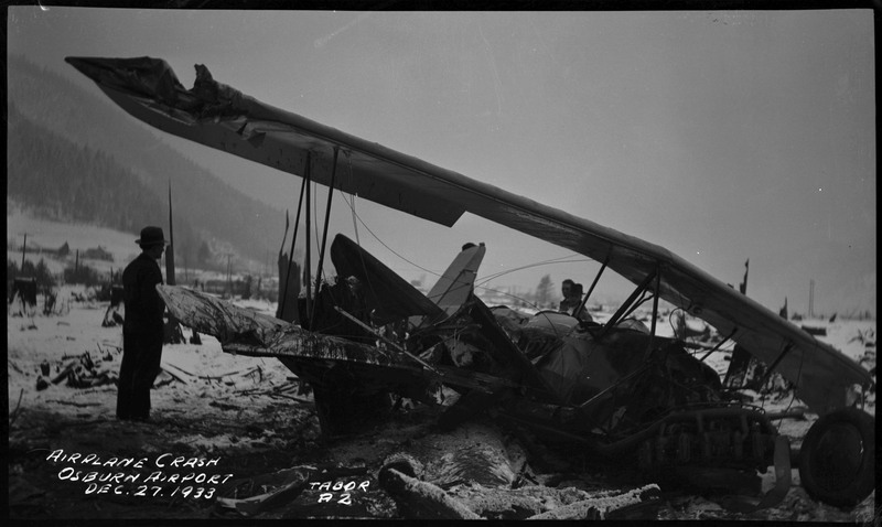 Three unidentified men stand near debris from an airliner crash. Caption on the bottom left of the photograph reads "Airplane crash Osburn Airport Dec. 27 1933."