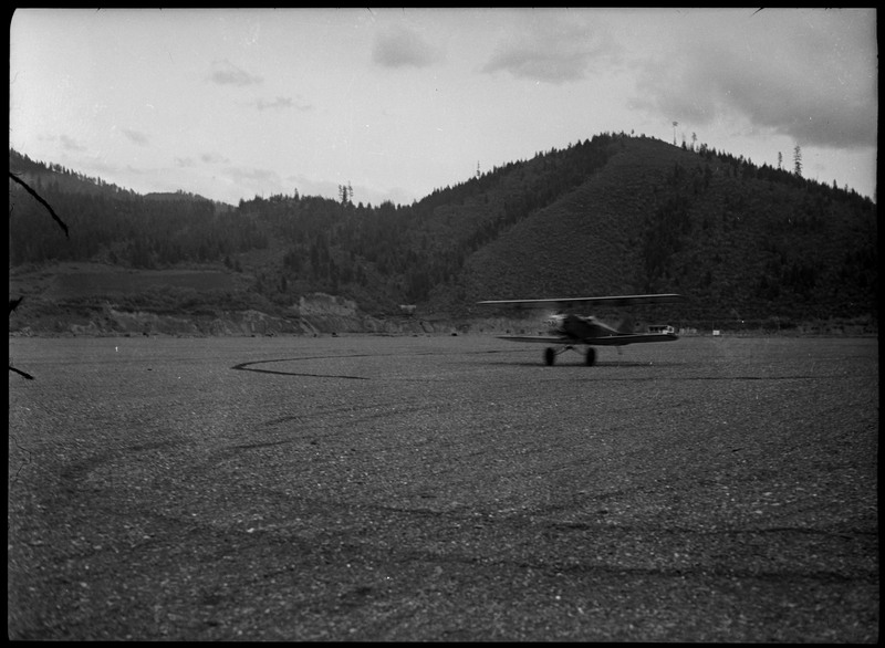 An airplane taking off in an empty field. A landscape of trees and mountains in the background.