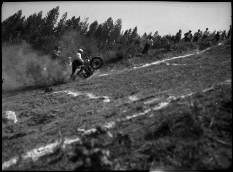 A man falling off his motorcycle during a hill climb. There are markings along the hill. Dust and dirt is flying in the air from the motorcycle.