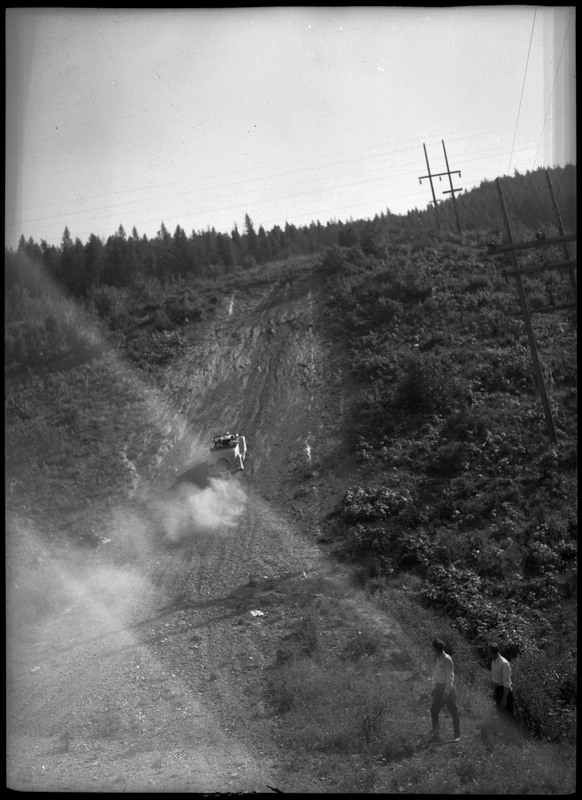 A car going up a hill during a motorcycle hill climb. Two people can be seen watching on the right of the image.