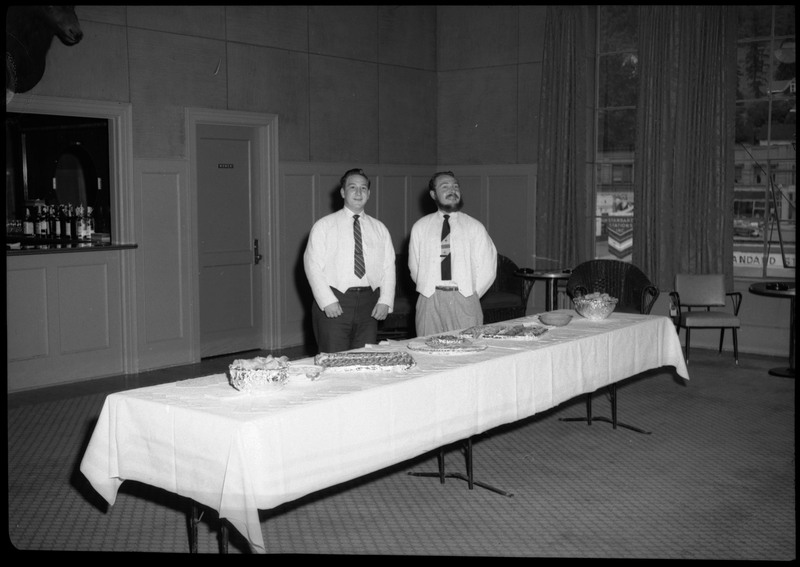 Two waiters standing behind a table during the Silver Jubilee banquet setup.