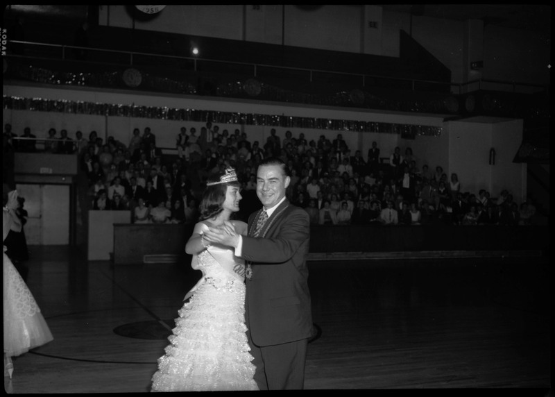 Two people dancing in a basketball court during the Silver Jubilee banquet. People are sitting on the bleachers in the background.