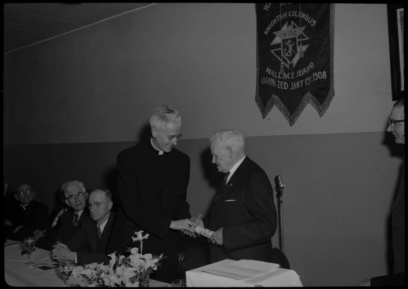 Two men shaking hands during a Knights of Columbus Jubilee event. Other people can be seen seated near the two men.