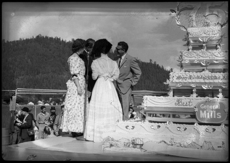 Four people standing on a stage near a large cake during the Silver Jubilee.