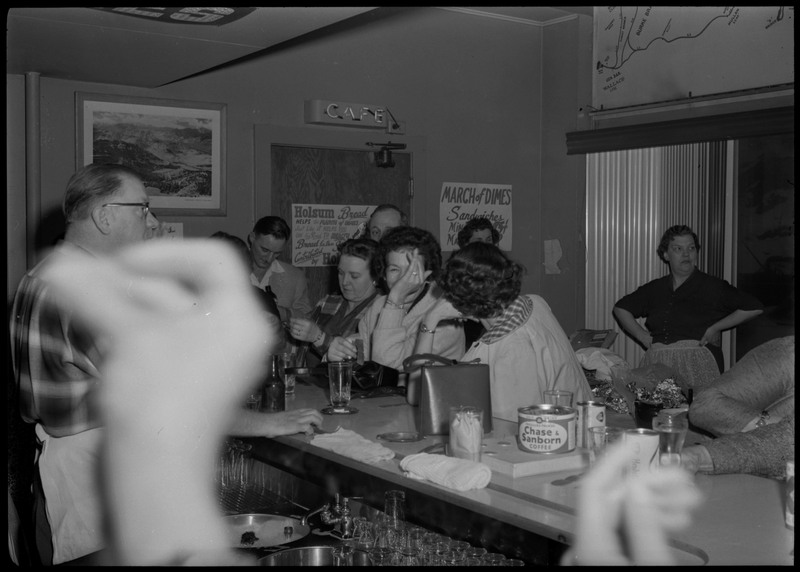 People sitting at a bar area during the Albie's March of Dimes event. Blurred hands appear in the foreground.