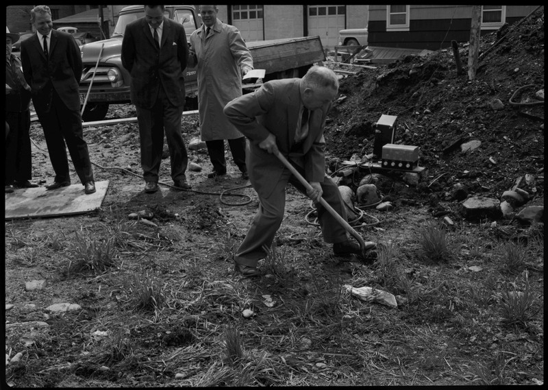 A man holding a shovel and digging as other men watch on during the Stardust Motel dedication.