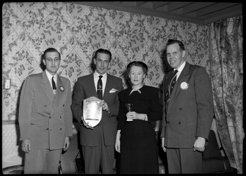 Three men and one woman posing during the Clerk of the Season awards ceremony. The woman and man in the center are holding awards.
