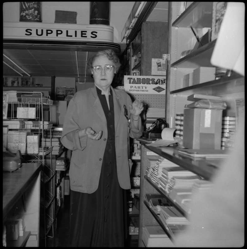A woman poses inside the Tabor store. There are office supplies and stationery on shelves around her.