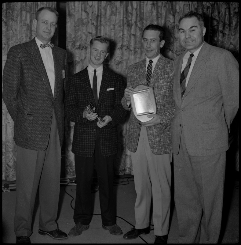 Four men posing during the Clerk of the Season awards ceremony. Two of the men standing in the center are holding awards.