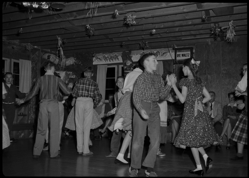People dancing at a dancing event in Wallace. Some people sitting along the walls. There are decorations adorning the room.
