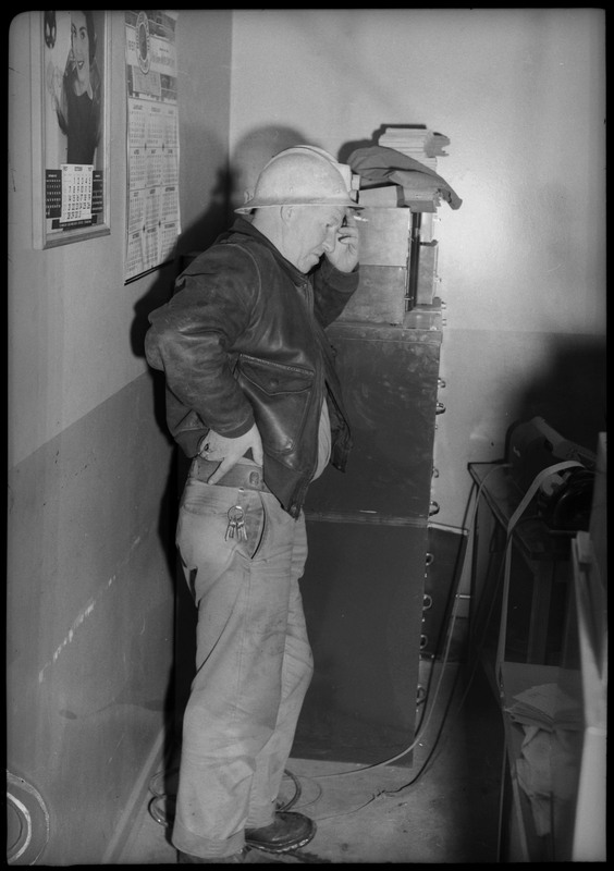 A man wearing a hard hat and holding a cigarette, leans against a file cabinet. Possibly at the Galena plant. 