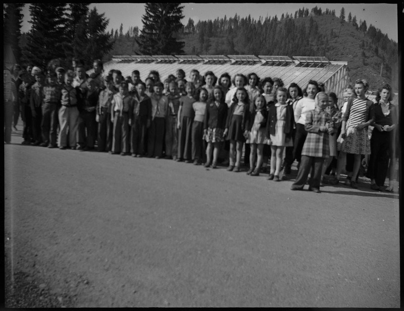 A group of children standing during Boys and Girls Week. There is a building with glass windows in the background.