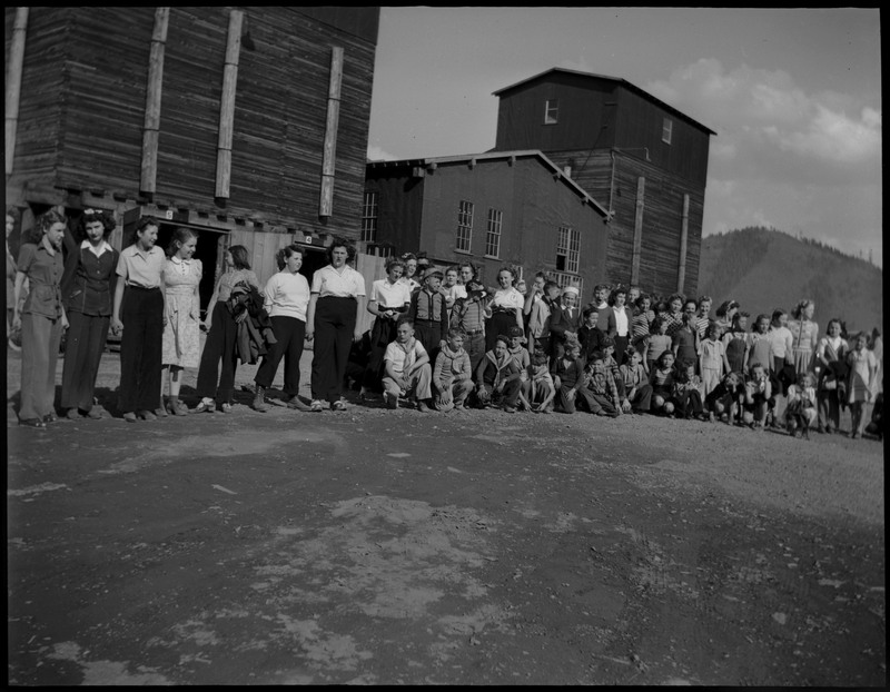 A group of children standing in front of several wooden buildings during Boys and Girls Week.