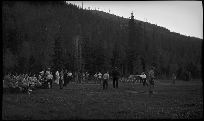 People gathered on a field for a police officers' picnic. Some people are sitting and watching, while others play in the field.