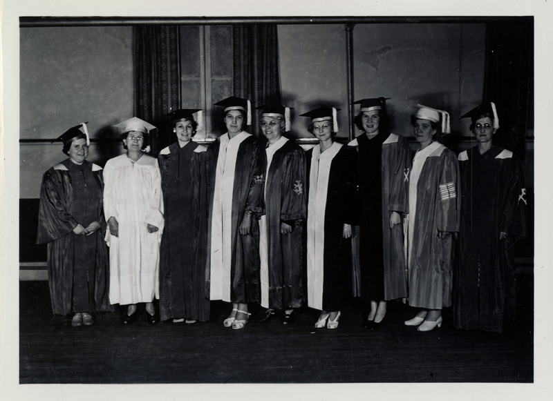 Nine unidentified female graduates standing wearing caps and gowns.