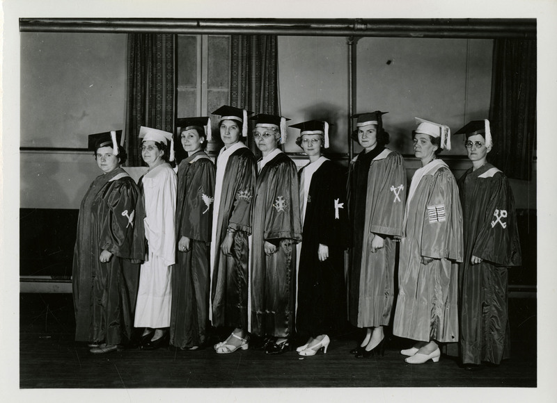 Nine unidentified female graduates standing wearing caps and gowns, facing towards the left.