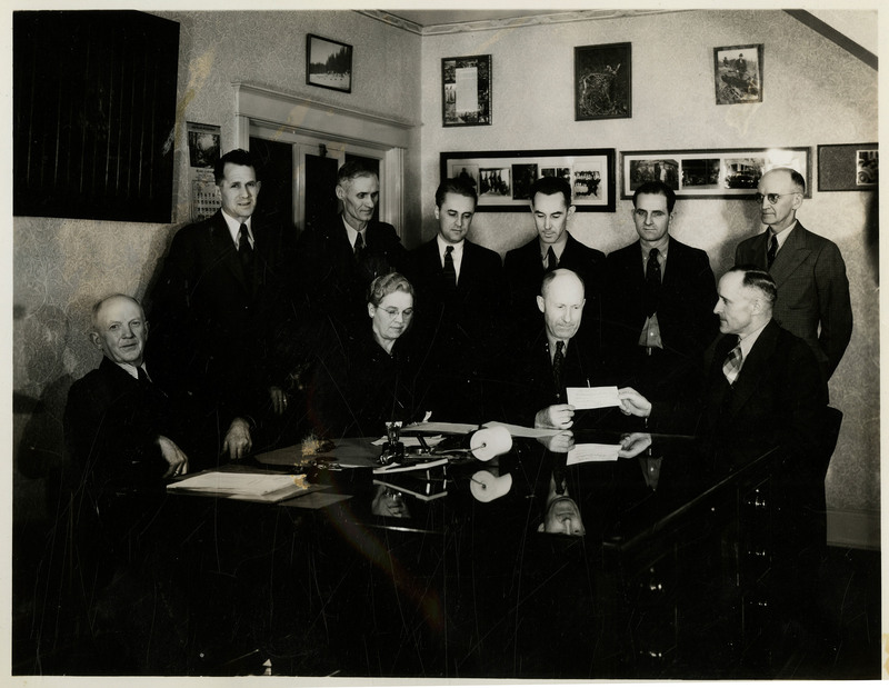 Men and one woman gathered around two men holding a check. Previously described as "Hatchery photo (payment for land)." Photo print for negative is 83-10-9.
