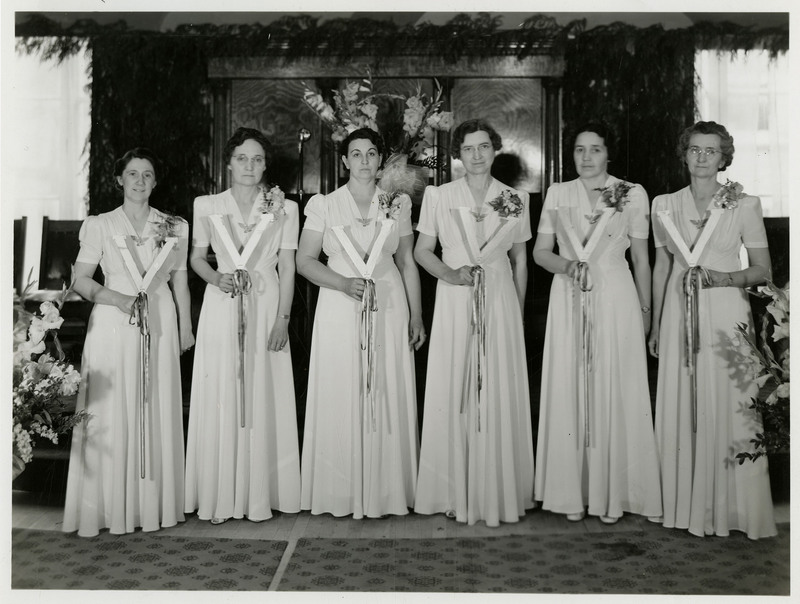 O.E.S. (Order of the Eastern Star of Idaho Grand Chapter) women pose for a photo. The women hold a V-shaped object with ribbons attached to the bottom.