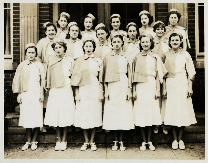 Theta Rho girl's drill team pose for a photograph, wearing matching uniforms and hats.