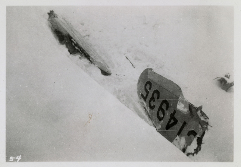 Remnants from an airliner crash mostly covered in snow. Numbers and letter "C14935" can be seen on the remnant.