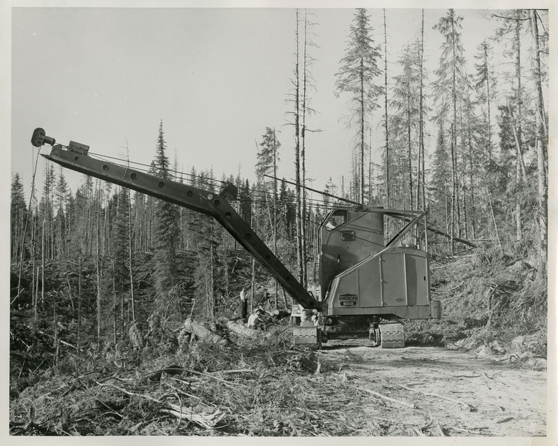 Several men stand and rest near logging machinery.