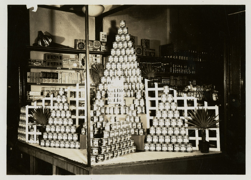 Display of cans of corn in the storefront of the Bennet's store on 5th Street, Wallace, Idaho. On verso "Photos of such displays were taken and then sent to manufacturer of the product, so the storekeeper could get a monetary rebate."