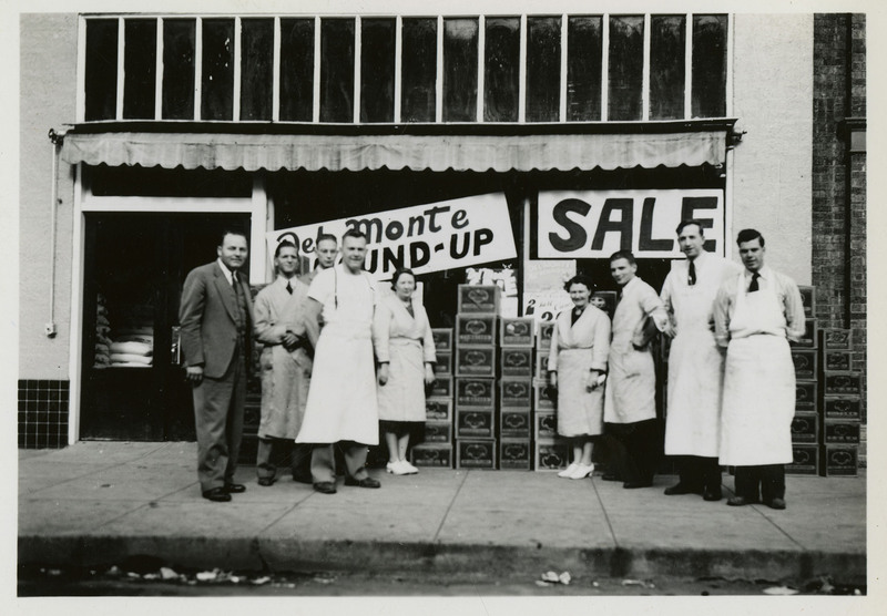 Workers stand in front of Table Supply store, Wallace. One sign says "Sale." Boxes line the front of the store.  