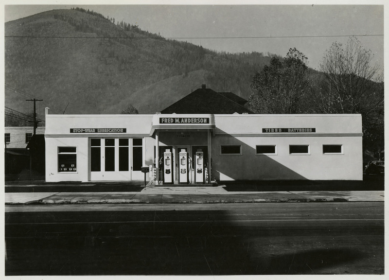 Union Oil Station and Bus Depot with signs on the building that read "Fred M. Anderson," "Stop-War Lubrication," and "Tires Batteries." Trees and mountains in the background.