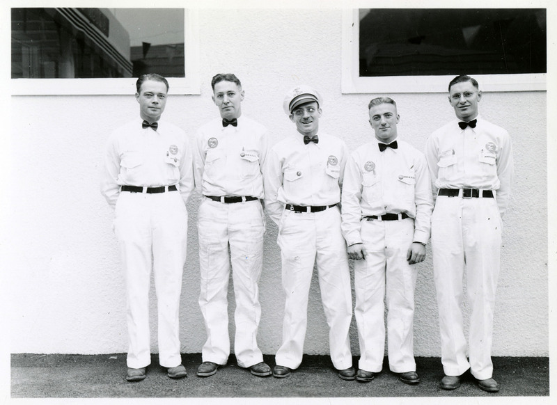 Two identified and three unidentified men in white uniforms and bow ties pose. The two identified men, starting from the right, are Tom Gellies and Jack M'Kay.