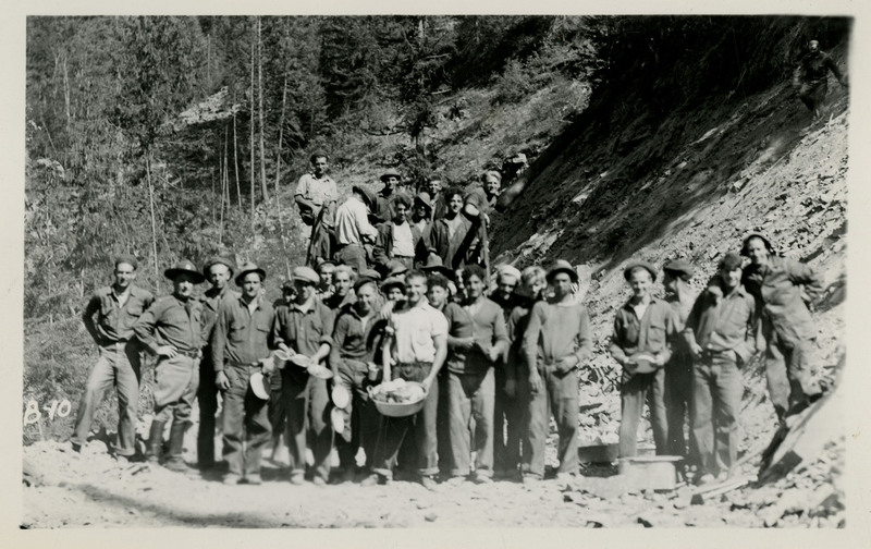 Civilian Conservation Corps members pose in front of rocky formation and trees.
