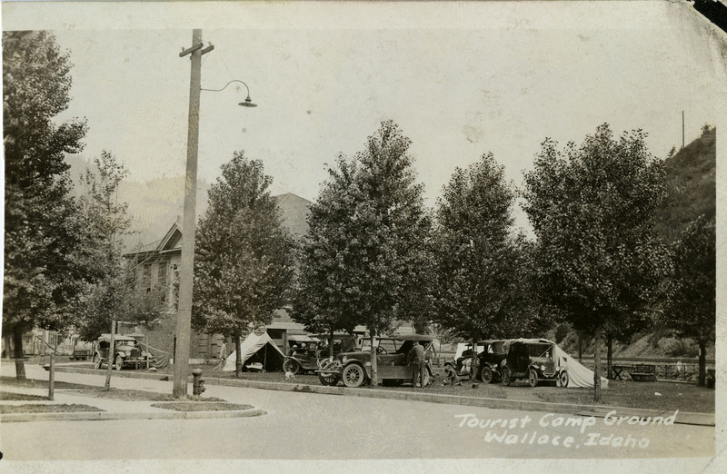 Postcard depicting the tourist campground in Wallace. Several automobiles parked on grass, some tents and two people can be seen.