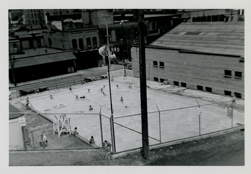 A view of the Wallace swimming pool. Several people are in the pool, while others sit and stand on the ledge.