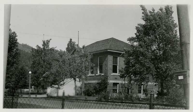 A view of the Wallace Carnegie Library which was completed in February/March 1911 and opened to the public on October 23, 1911. Part of a fence runs along the foreground. Trees can be seen in the distance.