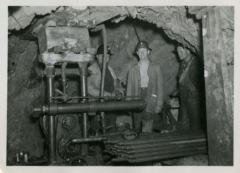 Three miners standing behind mining machinery.