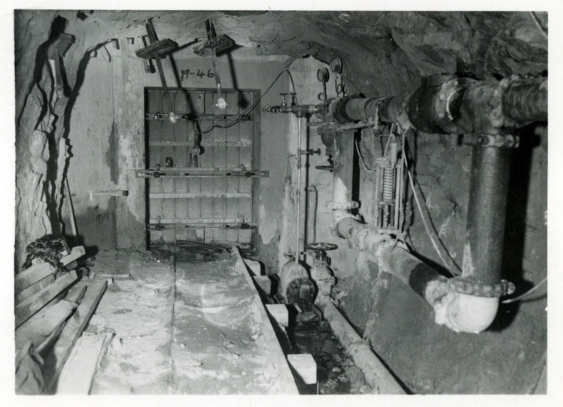 Photograph of a fire door in a mining tunnel. Pipes and mining equipment line the sides of the tunnel.