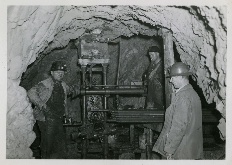 Three miners working with mining machinery.