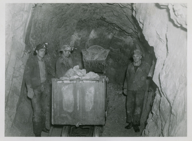 Three miners standing next to mine carts.