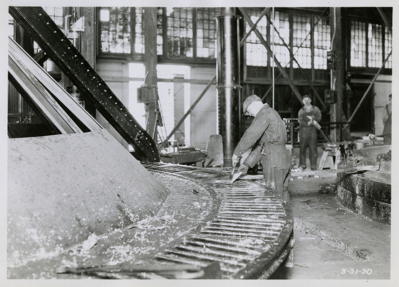 A man working on the lead casting machine. Two other workers can be seen in the background.