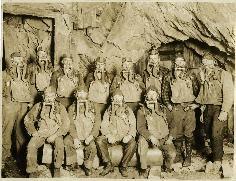 Miners pose wearing oxygen masks and tanks.