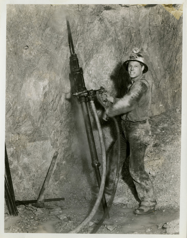 A miner holds mining machinery to drill into rock.