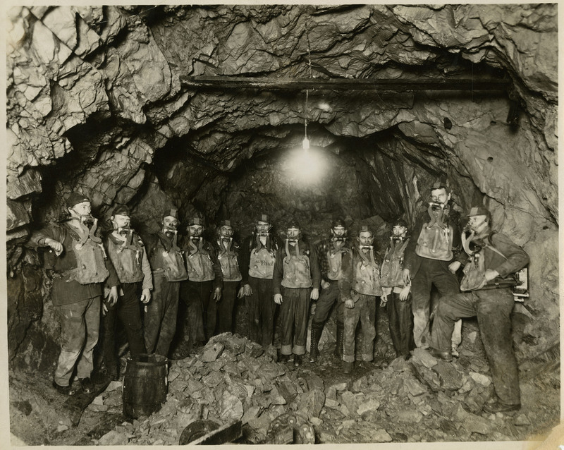 The Hecla Mine rescue crew pose inside a mine and wearing oxygen masks and canisters.