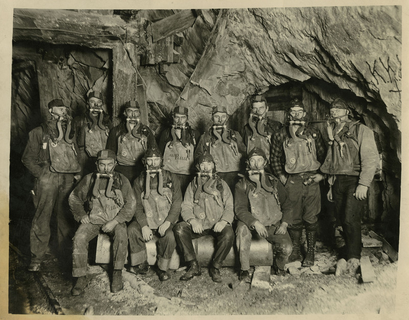 The Hecla Mine rescue crew pose inside a mine and wearing oxygen masks and canisters.