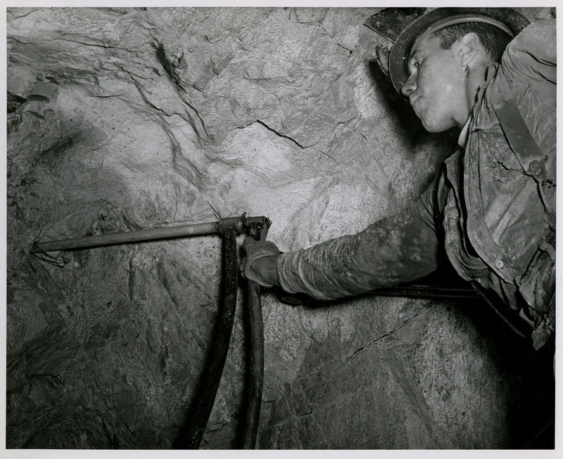 A miner uses a handheld drill to drill into rock.