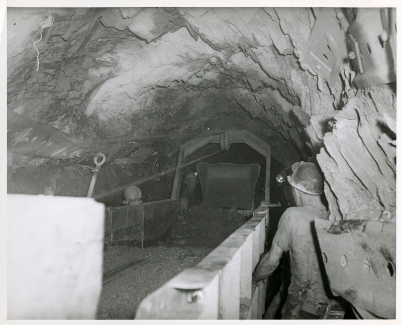 Miners working inside a mine, moving a mine cart of materials.