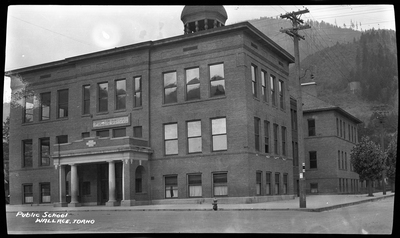 Photo of a public school building in Wallace, Idaho. The building is three stories tall and there is a sign that reads "Public School" above the front doors.