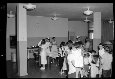 Photo of several unidentified people, mostly women and children, in line at the Shoshone County Polio Shot Clinic getting their vaccines. There are several nurses in the room administering shots.