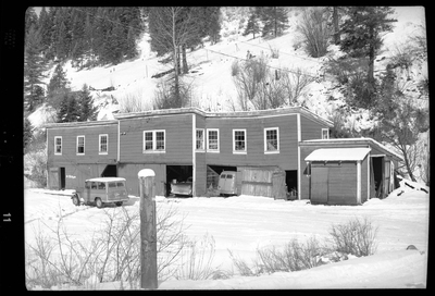 Photo of a building in the snow that has several garage door openings, with two cars parked inside of them. Described as "Standard Dairy, E. F. Gentry." There is a heavy layer of snow on the ground surrounding the building and the roof, as well as a third car parked outside of the building.