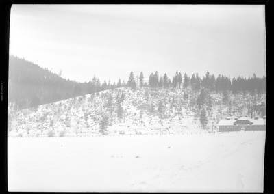 Photo of the city of Silverton, Idaho in the snow. A building sits off to the side in the photo, and a tree covered hill behind it. Everything is covered in snow.