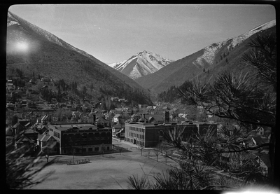 Photo overlooking the city of Wallace, Idaho. The photo was taken at a higher elevation than the city, where the city park and surrounding buildings are easily visible. The mountains that surround the city have a light layer of snow on the tops of them.