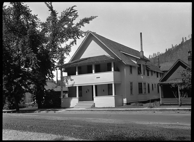 Photo of a home in Wallace, Idaho taken for Household Magazine. The house is two stories tall with a balcony for the second floor on the front of the house. There is a large tree in the front yard.